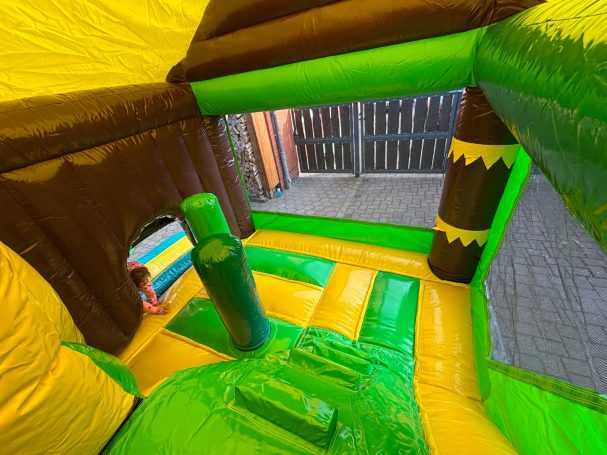 Bunte Hüpfburg mit grünen und gelben Elementen, einer Rutsche und Spielbereichen.