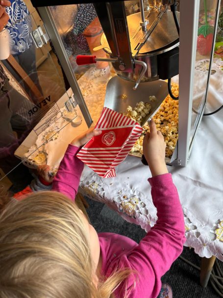 Ein Kind füllt Popcorn in ein rotes Streifenbecher an einem Popcornstand.
